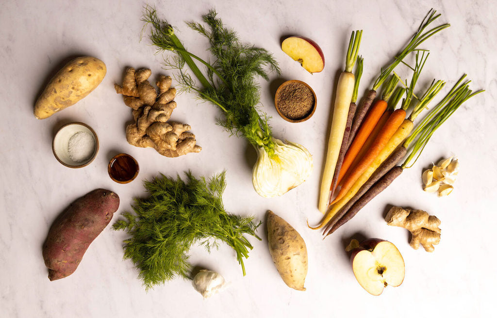 Carrots, vegetables, fruit and herbs laid out on a white surface